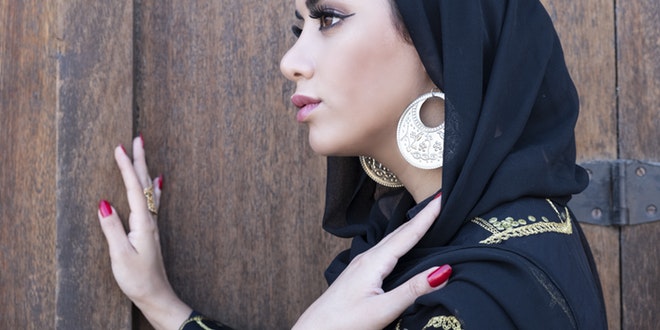 A woman wearing a black head scarf and earrings.