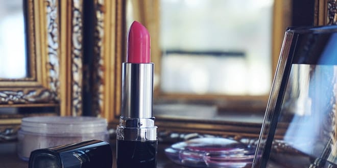 A pink lipstick sits on top of a mirror.
