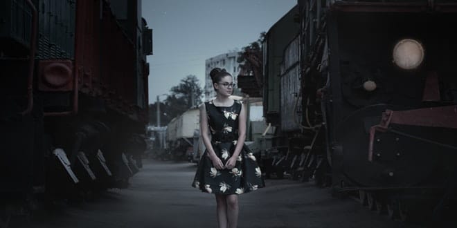 A girl in a black dress is standing in front of a train.