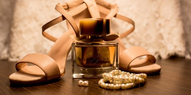 A bottle of perfume and a pair of high heeled shoes on a wooden table.