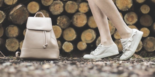The legs of a woman standing next to a backpack and logs.