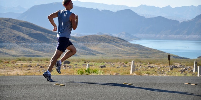 A man running on a road with mountains in the background.