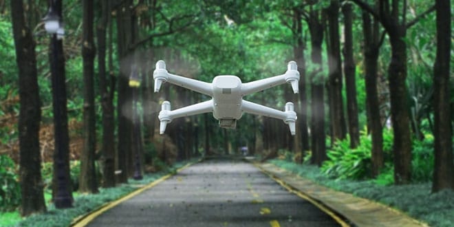 A white drone flying over a road in a forest.