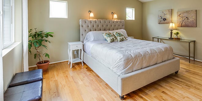 A bedroom with hardwood floors and a white bed.