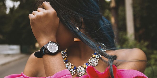 A woman with blue hair wearing a pink dress and a watch.