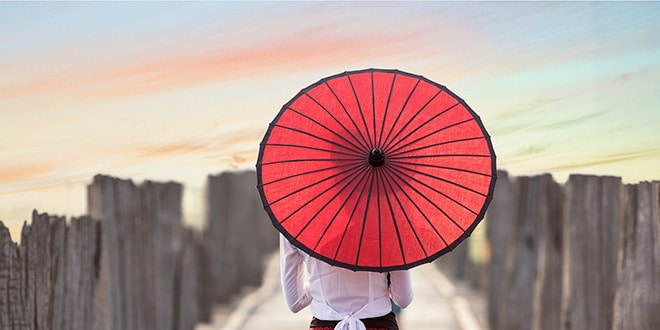A woman walking on a bridge with a red umbrella.