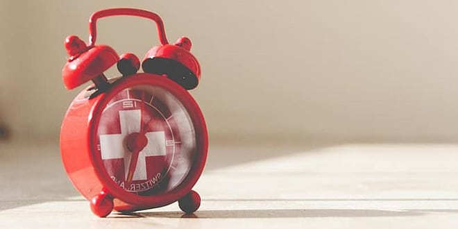 A red alarm clock with a swiss cross on it.