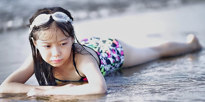 A young girl in a swimsuit laying on the beach.