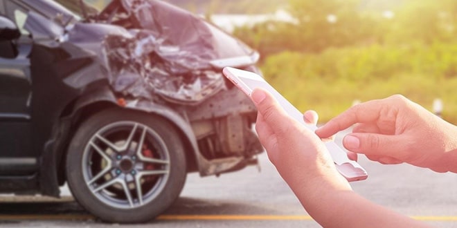 A person using a cell phone in front of a wrecked car.