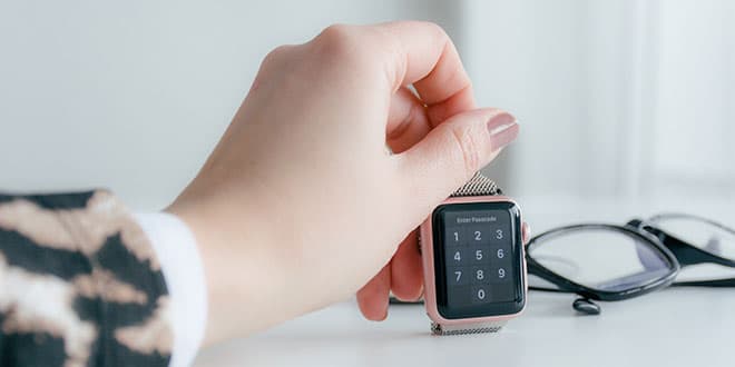 A woman's hand holding a smart watch on a desk.