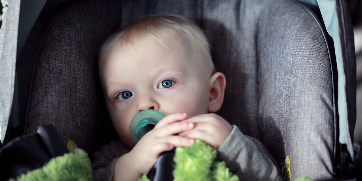 A baby in a car seat with a pacifier in his mouth.