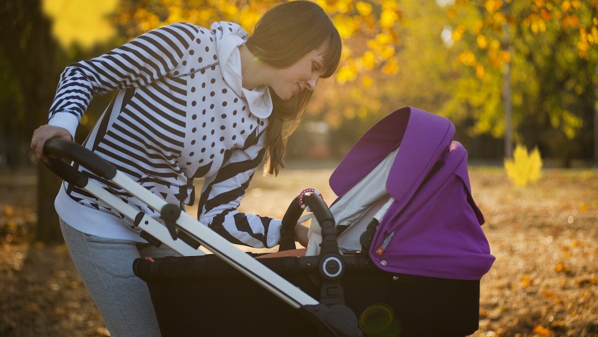 A woman looking at her baby while pushing a stroller in an autumn park.