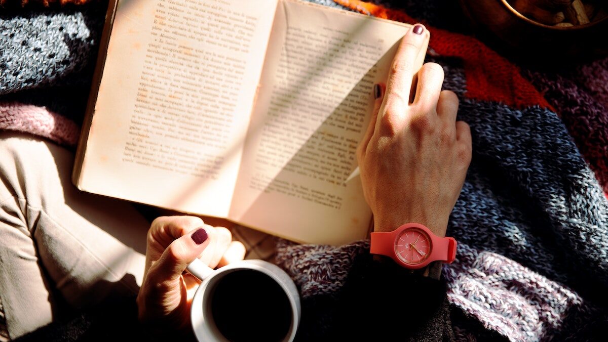A woman reading a book and holding a cup of coffee.