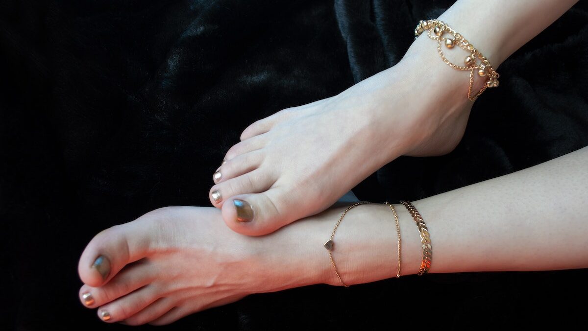 A woman's feet with precious golden anklet bracelets on them lying on black background.