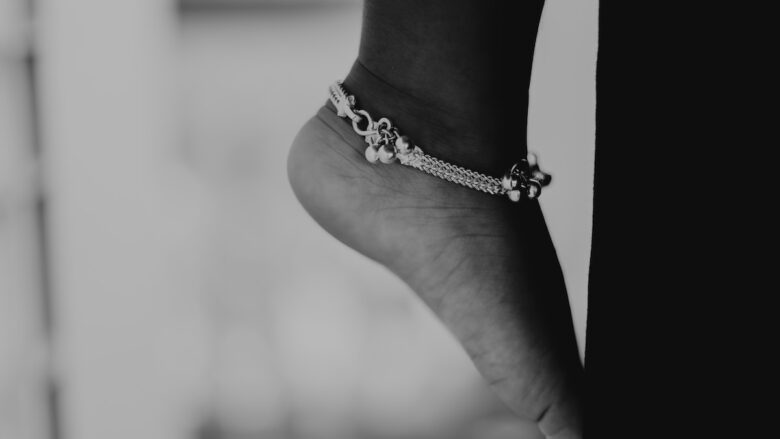 A black and white photo of a woman's foot wearing a anklet bracelet.