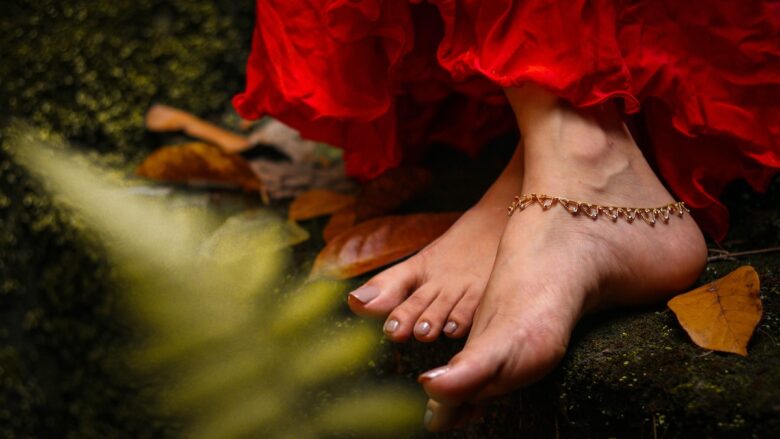 A woman wearing a red dress and gold anklet bracelet and bare feet.