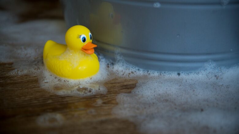 A rubber duck sitting next to a bucket of soap.