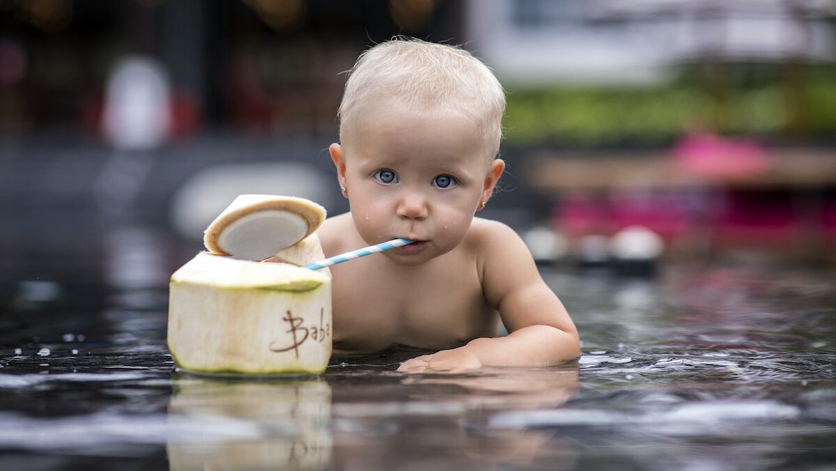A baby is drinking from a coconut in the pool.