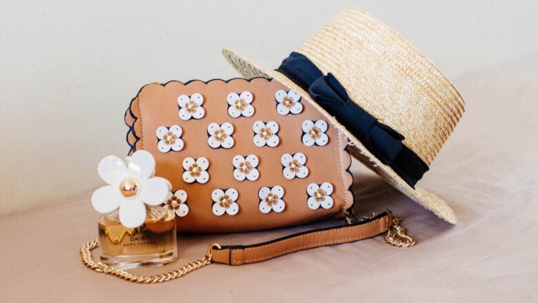 A brown sun hat, purse, and a flower on a table.