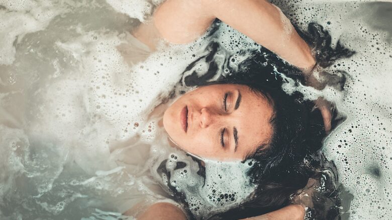 A woman is laying in a bath tub with bubbles.
