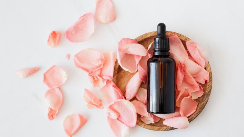 A bottle of rose essential oil with petals on a wooden plate.