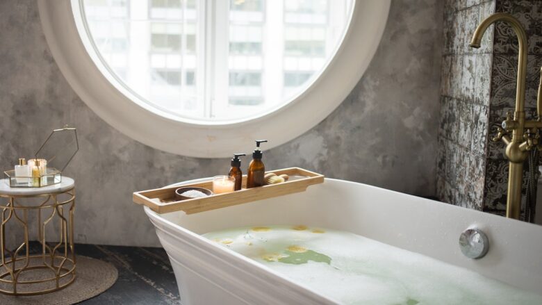 A bathtub with skincare supplies in a bathroom with a window.