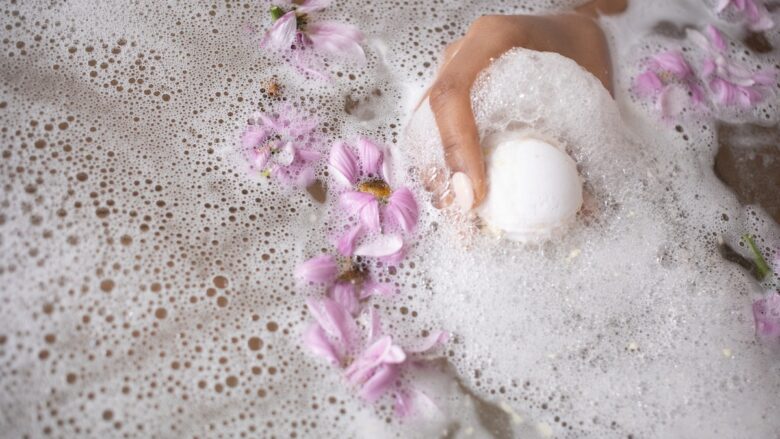 A woman is taking a bath with foam and flowers.