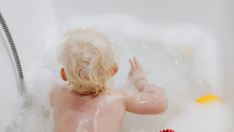 A baby playing with bubbles in a bath tub.