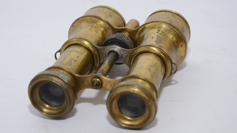 A pair of brass binoculars on a white surface.